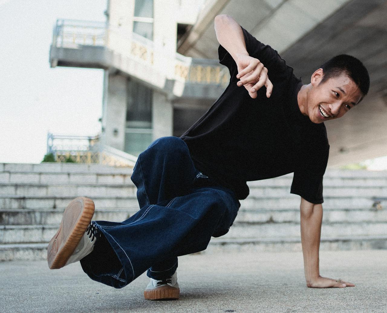 TOP Young Asian man breakdancing with vibrant energy outdoors on urban steps.