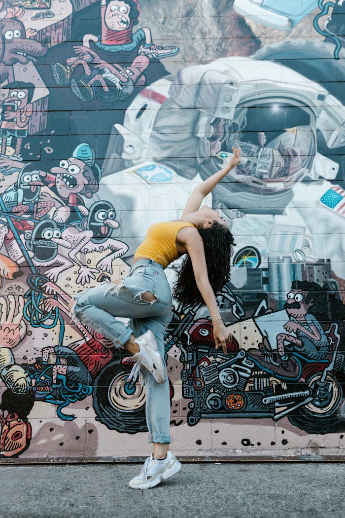TOP Woman performing contemporary dance against a colorful graffiti art mural, showcasing urban street style.