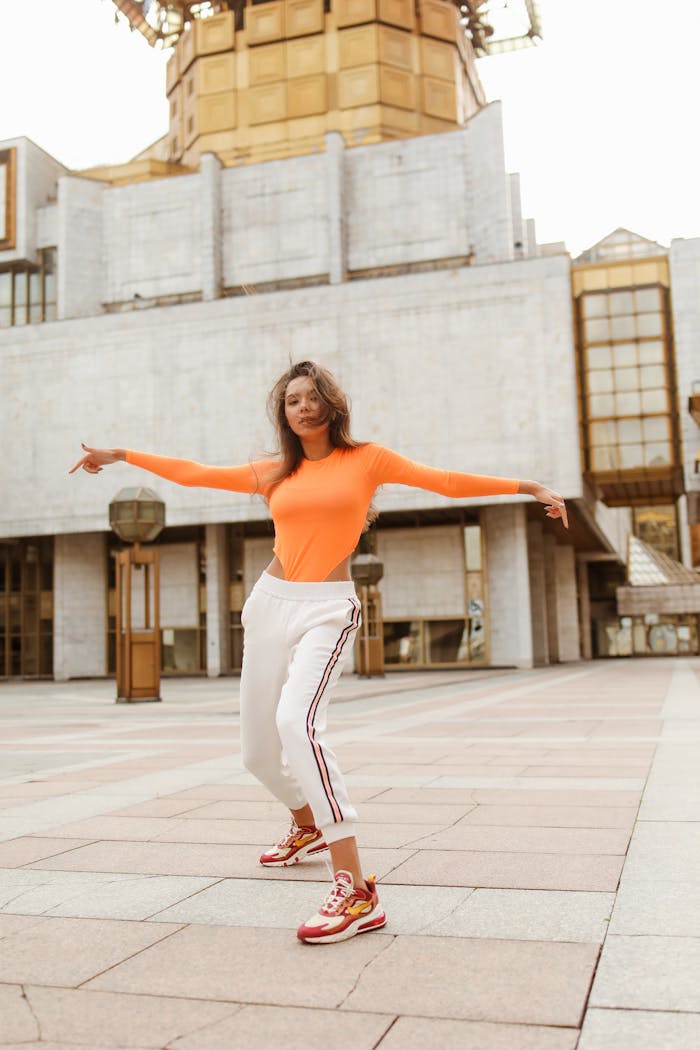 A woman in vibrant athletic wear dances joyfully in a modern cityscape.